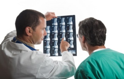 Doctors confer while examining film scans of patient's spine.